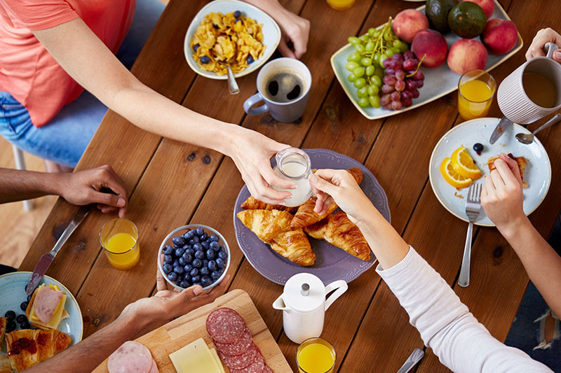 Mesa de brunch en casa con variedad de frutas, croissants, café y jugo de naranja compartida con amigos.