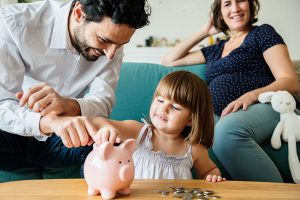 Una familia joven con una niña pequeña insertando monedas en una alcancía de cerdito rosa, representando el ahorro inteligente y los beneficios de los fondos de inversión colectiva.