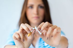 Mujer rompiendo decididamente un cigarrillo dejar de fumar con las manos enfocadas en primer plano y su expresión determinada desenfocada en el fondo.
