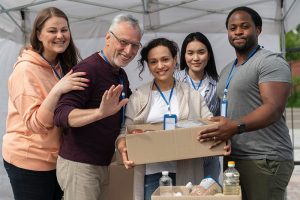 Grupo diverso del voluntariado corporativo de la Red de Solidaridad de Compensar sonriendo mientras sostienen cajas de donaciones durante una jornada de impacto social.