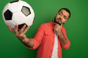 Hombre analizando un balón de fútbol con expresión de duda, ideal para ilustrar las curiosidades del mundial de futbol