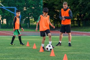 Entrenador supervisando a niños en un circuito con conos durante una práctica de fútbol formativo de LALIGA Schools Compensar.