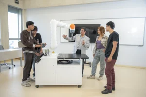 Estudiantes y docente en el laboratorio especializado de robótica industrial del nuevo campus de la UCompensar en Bogotá, operando un brazo robótico articulado.