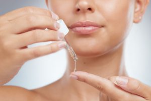 Mujer aplicando gotas de sérum de ácido hialurónico sobre la piel del rostro para hidratación facial