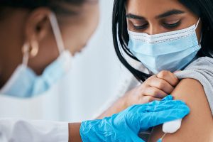 Profesional de la salud aplicando la vacuna contra la influenza en el brazo de una paciente protegida con mascarilla.