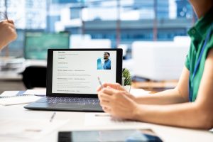 Reclutadora examinando perfil de LinkedIn y hoja de vida de solicitante en laptop