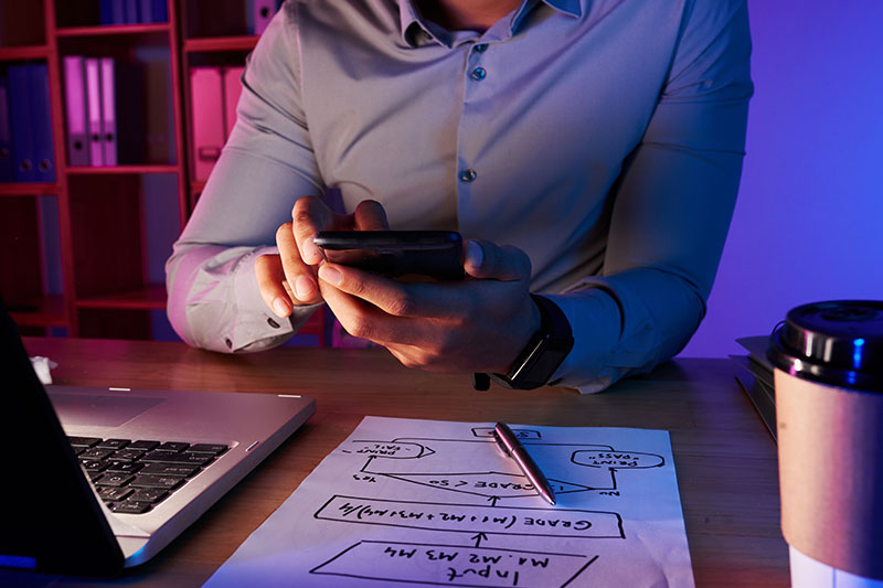 Profesional usando smartphone para integrar IA en el trabajo junto a esquema de planificación y café en escritorio.