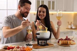 Pareja disfrutando de una fondue de queso con vino blanco durante una cena romántica en casa para celebrar Amor y Amistad.
