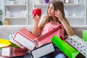 Mujer contemplando una alcancía rodeada de bolsas de compras compulsivas no planeadas.