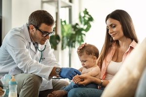 Médico de medicina prepagada Compensar examinando a un bebé en consulta a domicilio junto a su madre.