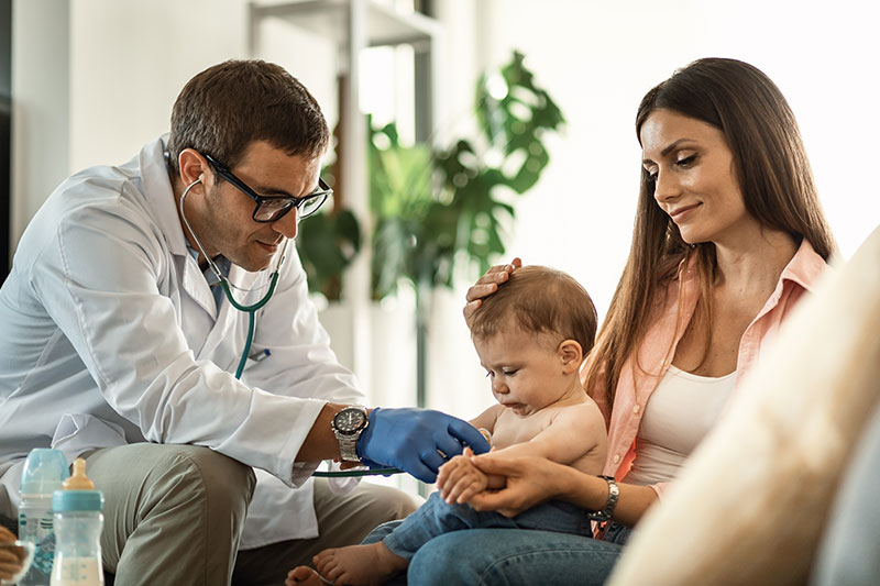 Médico de medicina prepagada Compensar examinando a un bebé en consulta a domicilio junto a su madre.